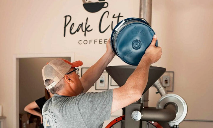 Man pours bucket of green coffee into hopper of 10 kilogram Mill City Roaster