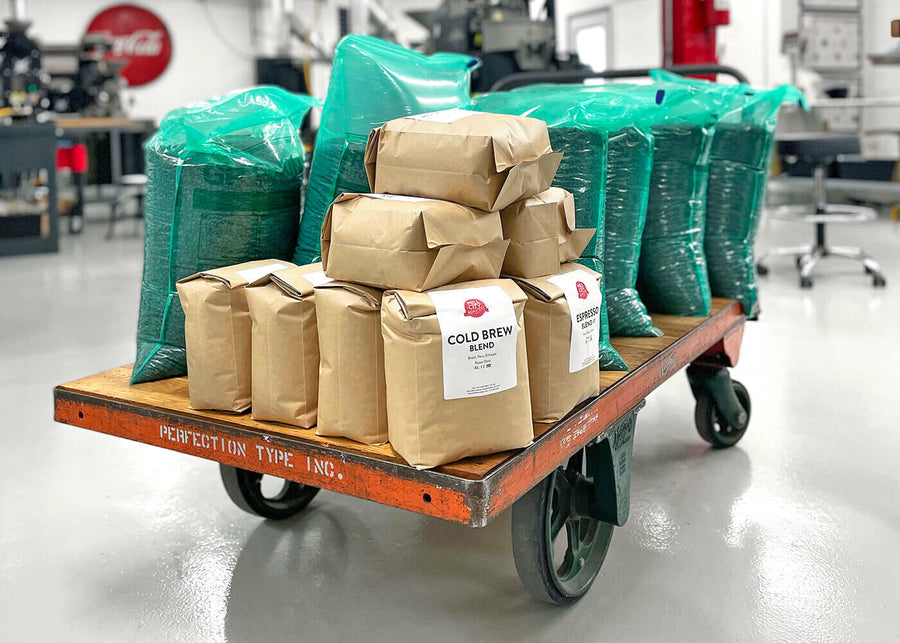 A rolling cart in a roastery with 5lb and 25lb bags filled with roasted coffee and labeled with coffee origin information