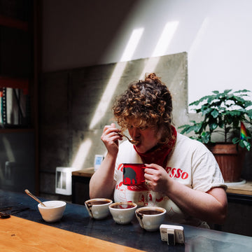 Person sipping coffee from a spoon in front of a row of coffee cups placed in a line on a table. 