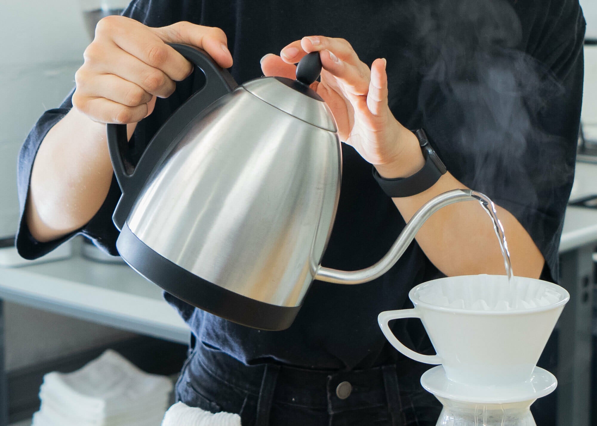 Someone is holding a kettle while pouring into a brewing device.