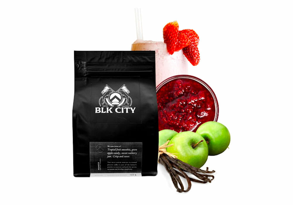 A bag of BLK City coffee sits on a white background. Green apples, vanilla beans, fruit jam and a strawberry milkshake are pictured to represent the flavor notes.