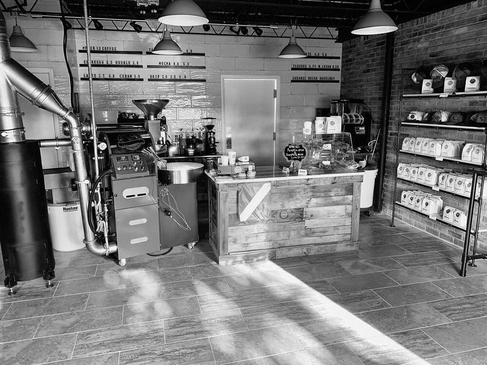 There is a roaster to the left of what looks to be a cafe space. There is a shelf to the very right with coffee bags and brewing equipment. In the middle there is a small kiosk with pastries.