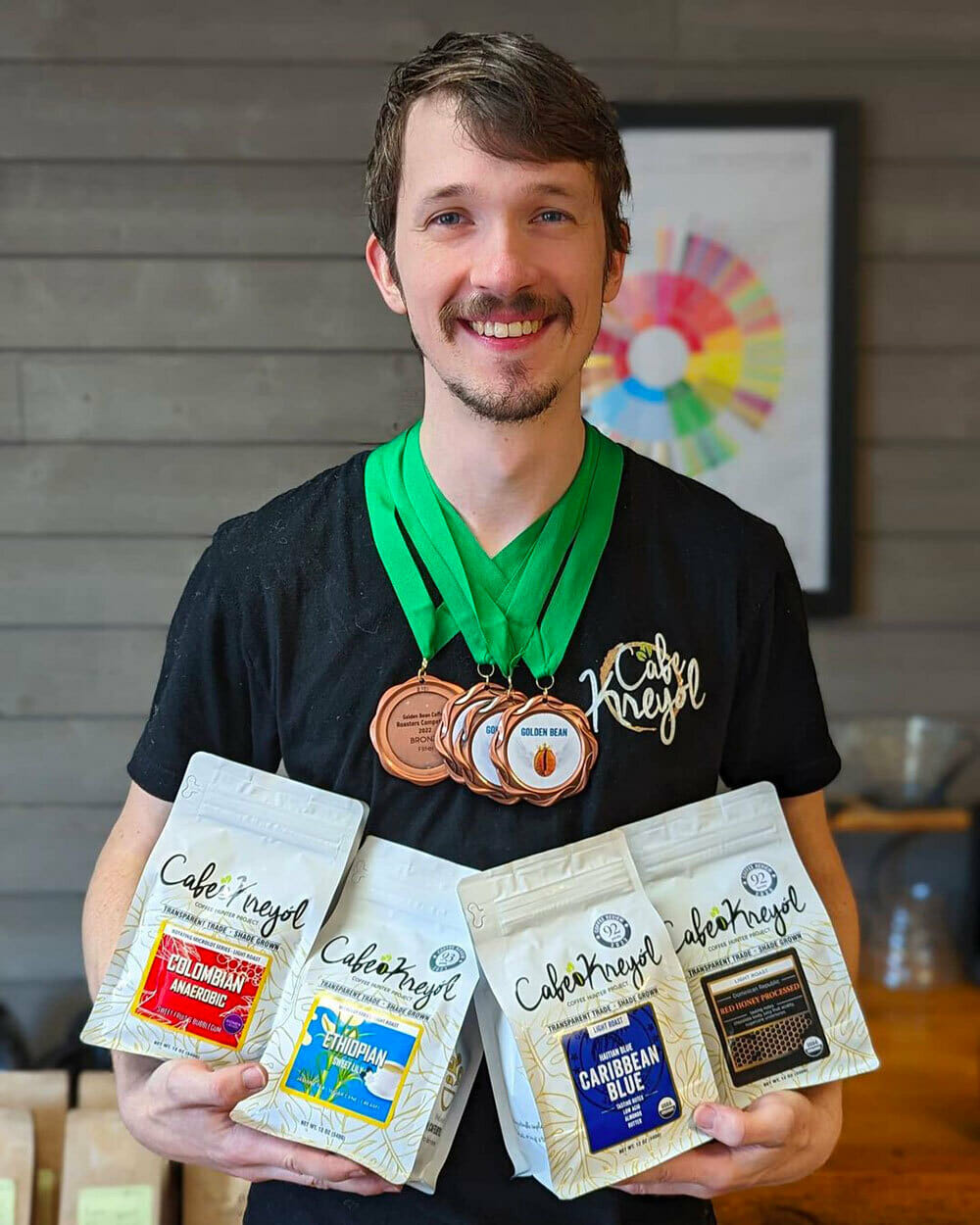 Someone wearing several medals while holding various bags of their own roasted coffee.