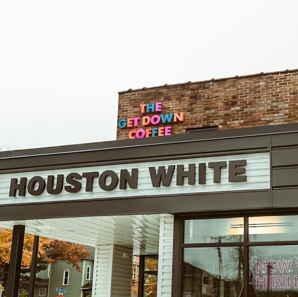 A building with the text "Houston White" in black. Just behind that, there is a brick building with the cafe space, The Get Down Coffee, right next to it.