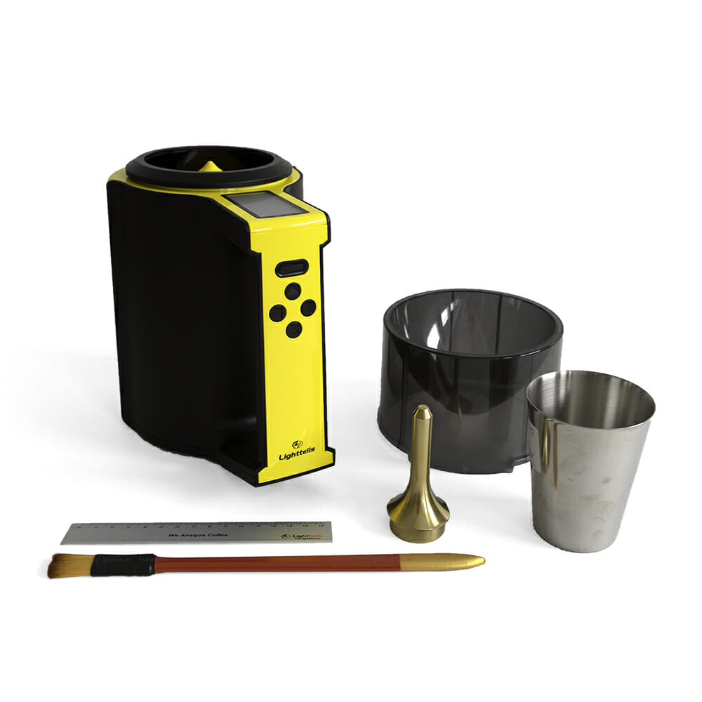 In front of a white background are a set of tools for coffee density readings. There is a pitcher-like device with a yellow handle and trim where the coffee sits inside. On the handle facing up there is a small screen where readings of the coffee are displayed. To the right of the image are two containers. One a small metal cup, and the other a plastic black almost transparent funnel device. Just in front of that is a gold weight that's used to release the coffee through the funnel and into the reader. In the front, there is a metal ruler and a red handled brush with a yellow tip.