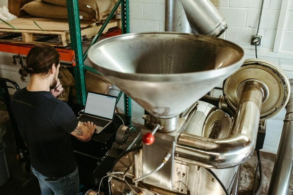 A shot of the top of the roaster. There's someone standing next to it working on a laptop.