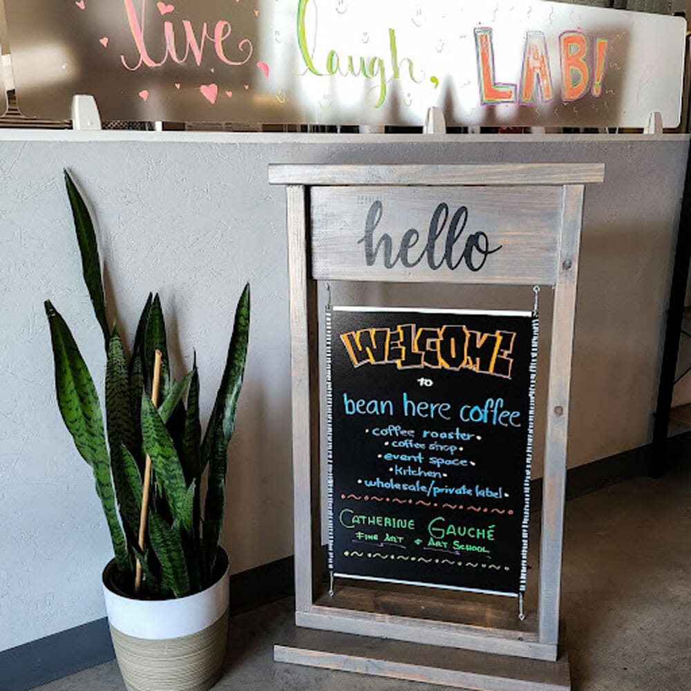 A plant and welcome sign positioned next to the entrance of a cafe.