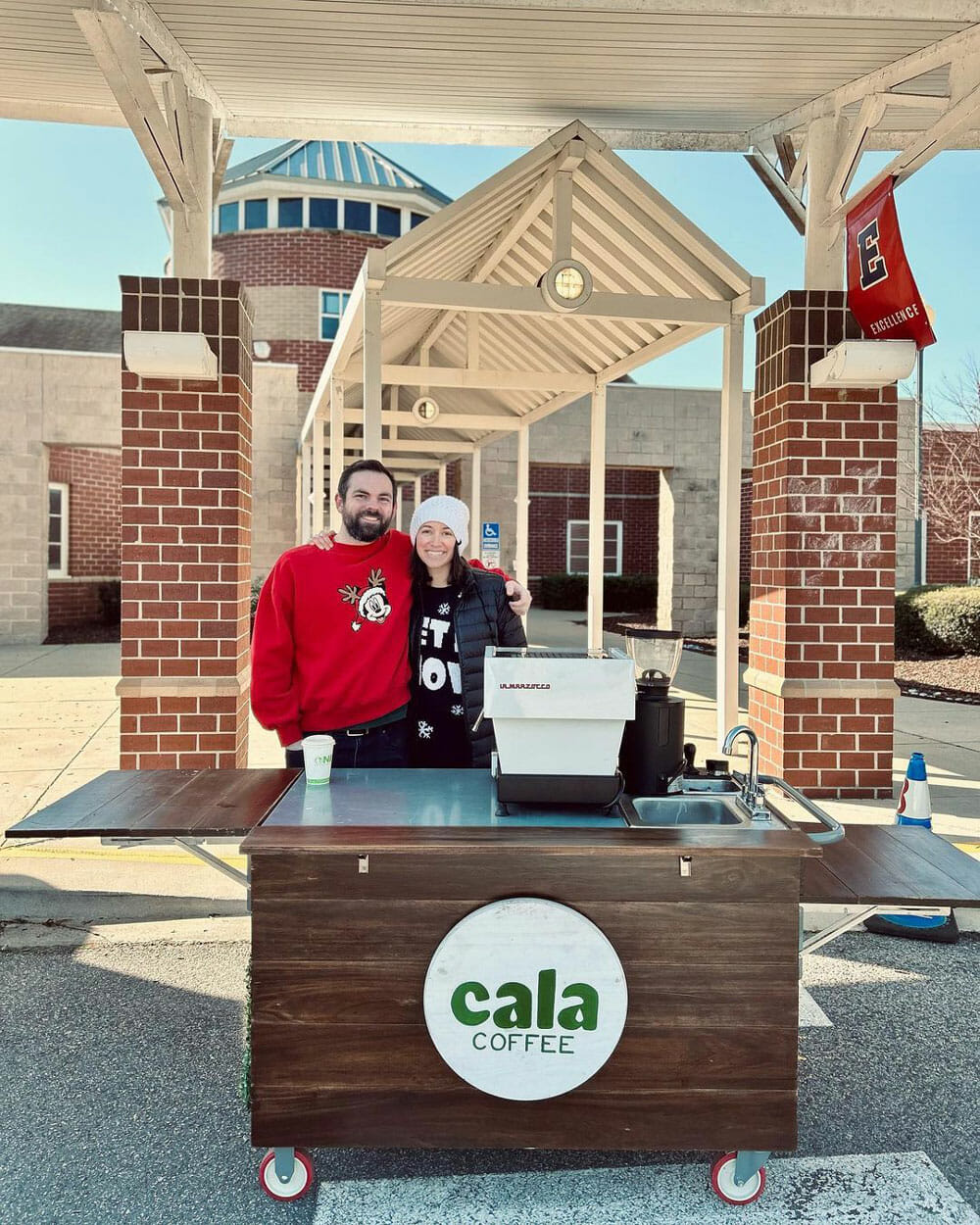 A couple stand behind a coffee cart. They are smiling at the camera.