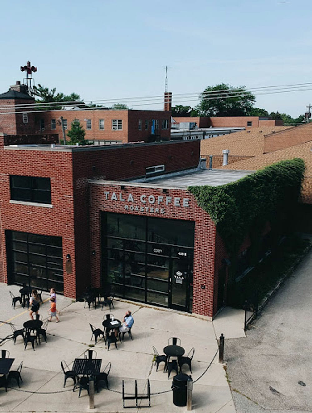 An aerial view of a cafe located inside of a large brick building with black patio tables and chairs outside.