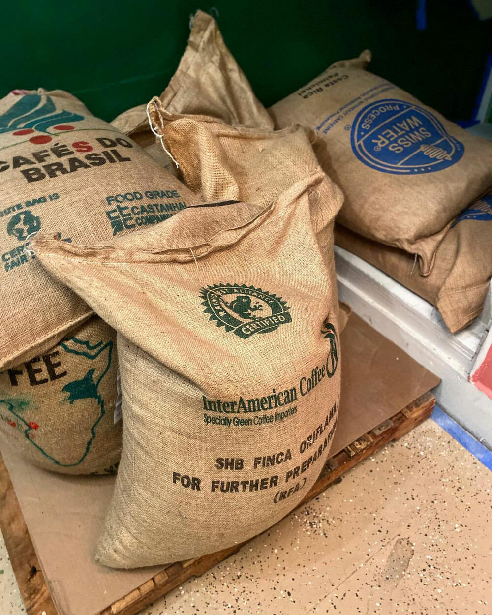 Several burlap bags of coffee lying on wooden pallets.