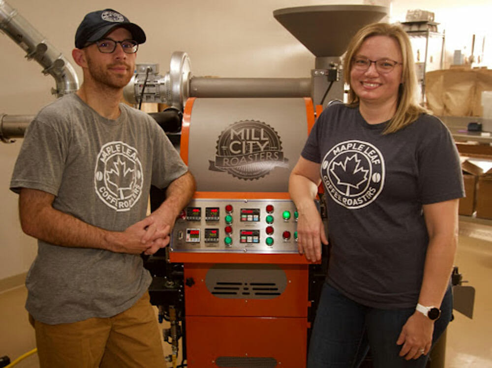 Two people standing in front of an orange roaster.